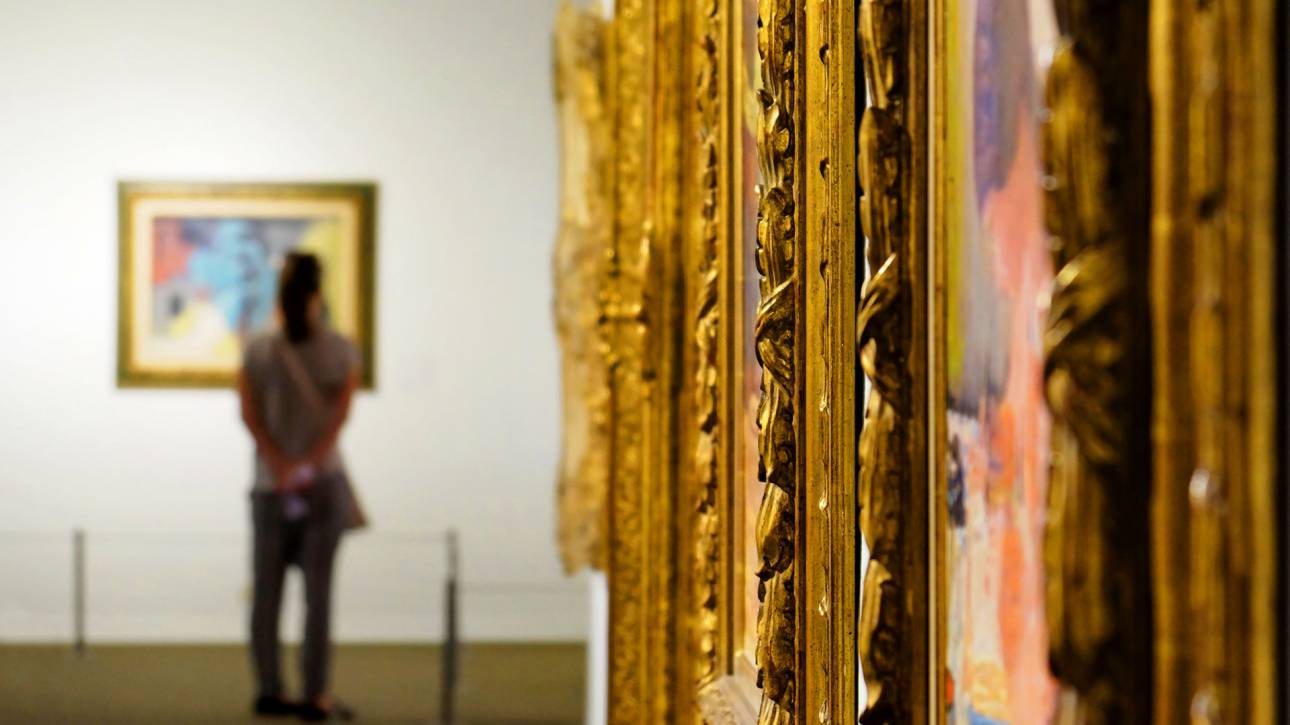 Ornate golden picture frames in an art gallery with a visitor viewing artwork in the background