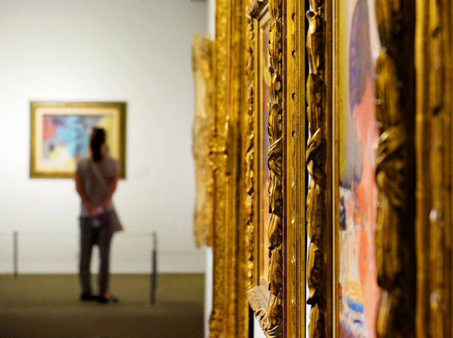 Ornate golden picture frames in an art gallery with a visitor viewing artwork in the background